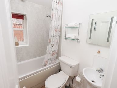 A small bathroom with a bathtub shower combination a toilet a sink a mirror and shelves with towels at Number Twenty in Keswick