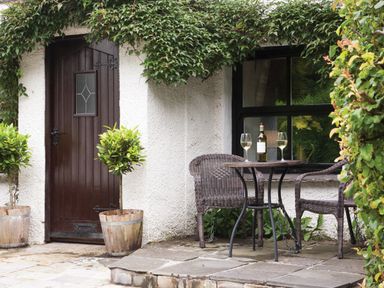 An outdoor patio with two wicker chairs around a small table holding a bottle and two wine glasses at Burrow Cottage in Bowness