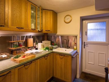 A kitchen with wooden cabinets a countertop with vegetables a sink and a door at Burrow Cottage in Bowness