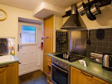 A kitchen with wooden cabinets a stove oven toaster kettle and a door at Burrow Cottage in Bowness