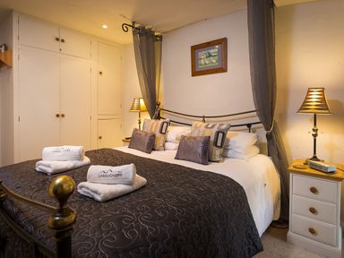 A bedroom with a bed covered with a dark quilt and folded towels on top with nightstands and lamps at Burrow Cottage in Bowness