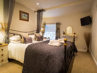 A bedroom with a double bed and pillows bedside tables with lamps a wall mounted television and a vanity at Burrow Cottage in Bowness