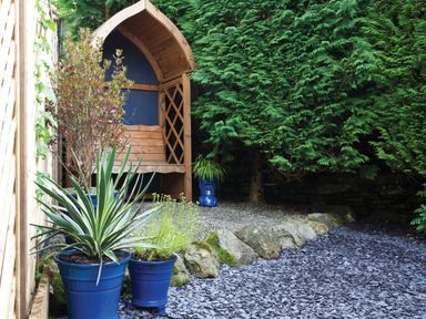 A garden area with blue plant pots gravel stones and a wooden bench at Burrow Cottage in Bowness