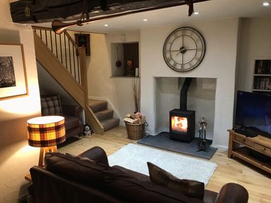 A living room with a wood burning stove and a large clock above it at Burrow Cottage in Bowness