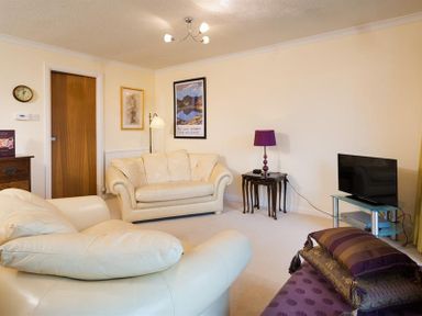 A living room with cream leather sofas a purple lamp a TV on a glass stand and framed pictures on the walls at Mount Sol in Ambleside