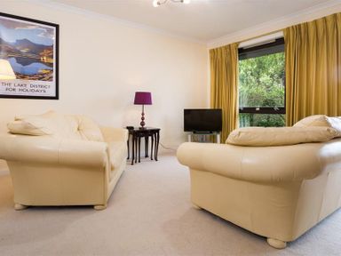 A living room with two cream sofas a small black table with a purple lamp a television and yellow curtains at Mount Sol in Ambleside