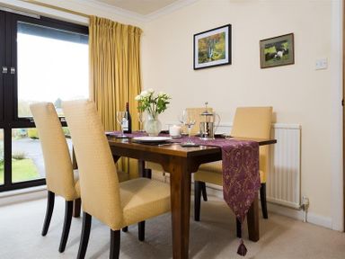 A dining room with a wooden table set with glasses and a vase of flowers at Mount Sol in Ambleside