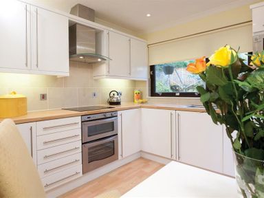 A kitchen with white cabinets a built in oven electric stove and flowers on a table at Mount Sol in Ambleside