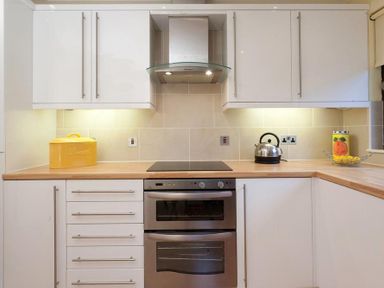 A kitchen with white cabinets a wooden countertop a stainless steel oven a kettle a yellow bread box and a glass fruit bowl at Mount Sol in Ambleside