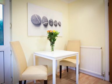 A small dining area with a white table, two beige chairs, a vase with flowers, and a wall painting of stones at Mount Sol Ambleside