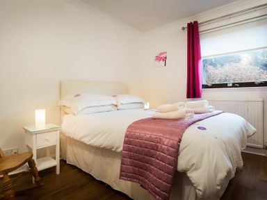A bedroom with a double bed white bedding pink throw and folded towels beside a window with red curtains at Mount Sol in Ambleside
