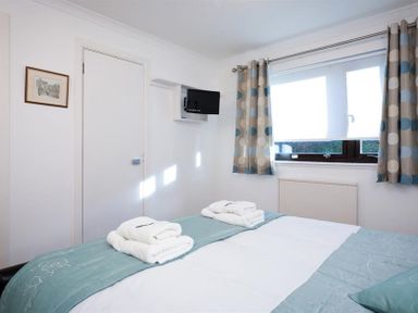 A bedroom with a bed with folded towels a window with patterned curtains and a wall-mounted television at Mount Sol in Ambleside