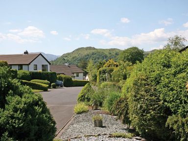 A street with houses and trimmed bushes next to a gravel path in a residential area at Mount Sol in Ambleside