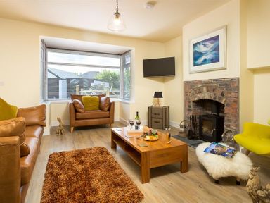 A living room with leather sofas a wooden coffee table a brick fireplace and a window at Greengarth in Keswick