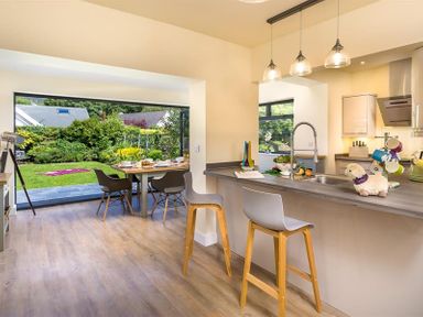 A kitchen with a breakfast bar and stools next to a dining table by a garden at Greengarth in Keswick