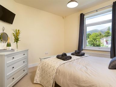 A bedroom with a bed with folded towels a chest of drawers and a window with curtains at Greengarth in Keswick