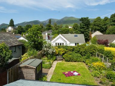 A garden with a shed a bench and a blanket on the grass with houses and hills in the background at Greengarth in Keswick