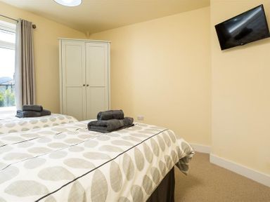 A bedroom with two beds a wardrobe a window with curtains and a wall-mounted television at Greengarth in Keswick