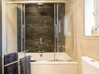 A bathroom with a bathtub and glass shower screen and black tiled wall at Greengarth in Keswick