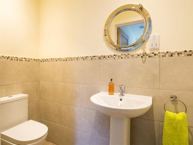 A bathroom with a toilet a pedestal sink a round mirror a soap dispenser and a towel on a ring at Greengarth Keswick