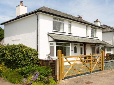 A white two-story house with a grey roof and wooden gate surrounded by greenery at Greengarth in Keswick
