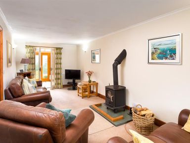 A living room with leather sofas a wood stove a TV and a basket of firewood at Garden Cottage At Coniston in Coniston