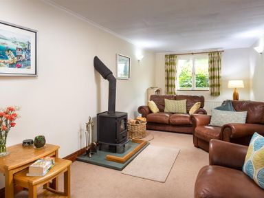 A living room with leather sofas a wood burning stove and side tables at Garden Cottage At Coniston in Coniston