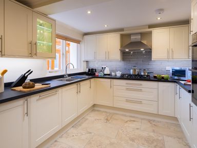 A kitchen with beige cabinets black countertops a stove with pots a microwave and a sink with a window at Garden Cottage At Coniston in Coniston