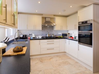 A kitchen with white cabinets black countertops a stove and oven and various kitchen items at Garden Cottage At Coniston in Coniston
