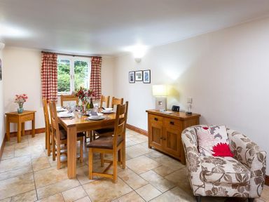 A dining room with wooden table and chairs a patterned armchair and wooden sideboards at Garden Cottage At Coniston in Coniston