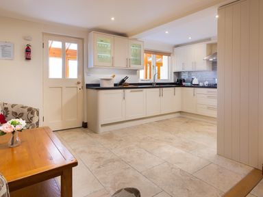 A kitchen with white cabinets a door a wooden table and tiled floor at Garden Cottage At Coniston in Coniston