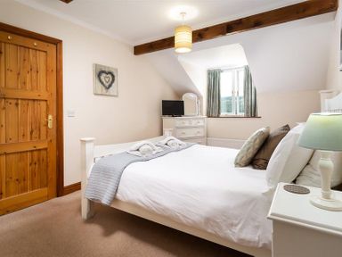 A bedroom with a white bed and pillows beside a wooden door and dresser at Garden Cottage At Coniston in Coniston