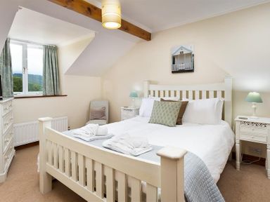 A bedroom with a white bed wooden frame bedside tables and a window with curtains at Garden Cottage At Coniston in Coniston