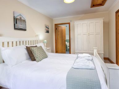 A bedroom with a double bed with pillows and folded towels a bedside table with a lamp a white wardrobe and wooden doors at Garden Cottage At Coniston in Coniston