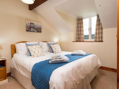 A bedroom with a bed with blue and white bedding and pillows next to a window with curtains at Garden Cottage At Coniston in Coniston