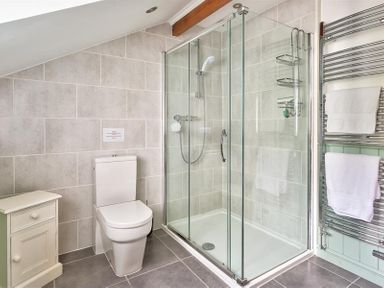 A bathroom with a toilet shower enclosure towels on a rack and a small cabinet at Garden Cottage At Coniston in Coniston