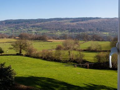 A countryside view with green fields trees and a lake in the distance at Garden Cottage At Coniston