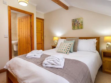 A bedroom with a double bed two bedside tables lamps and a painting above the bed at Garden Cottage At Coniston in Coniston