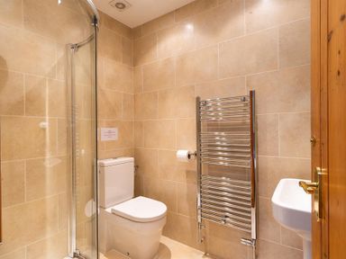 A bathroom with a toilet shower with glass door chrome towel radiator and white sink at Garden Cottage At Coniston in Coniston
