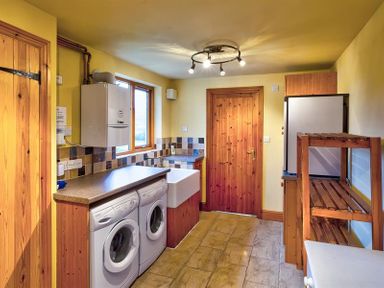 A laundry room with a washing machine and dryer under a counter a sink and wooden doors at Garden Cottage At Coniston in Coniston