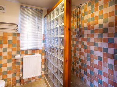 A bathroom with a tiled shower area separated by glass blocks and a window with blinds at Garden Cottage At Coniston in Coniston