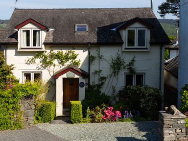 A front view of a two-story white cottage with shrubs and flowers at Garden Cottage At Coniston
