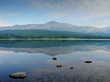 A lake with rocks in the water and mountains reflected in the lake at Garden Cottage At Coniston in Coniston