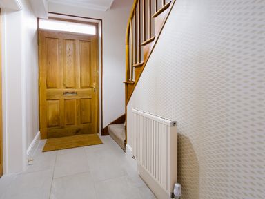 An entryway with a wooden front door a carpeted staircase and a wall-mounted radiator at Pippin Cottage in Keswick