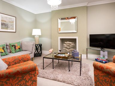 A living room with patterned orange chairs a glass coffee table a gray sofa and a television at Pippin Cottage in Keswick