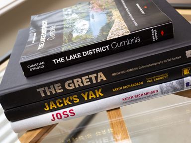 A stack of four books about Cumbria on a glass table