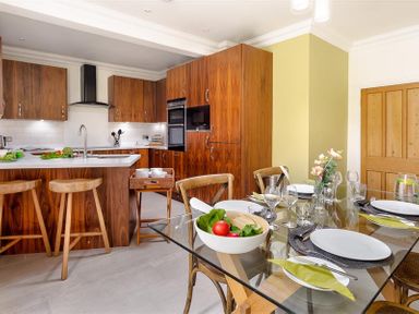 A kitchen with wooden cabinets and stools and a dining table set with plates and glasses at Pippin Cottage in Keswick