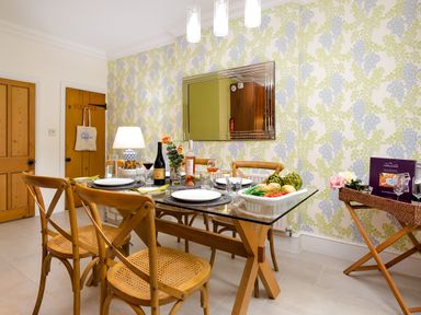 A dining room with a glass table set for four with wooden chairs and patterned wallpaper at Pippin Cottage in Keswick
