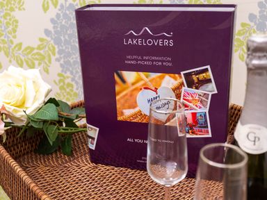 A wicker tray with a white rose purple folder two empty wine glasses and a bottle of Prosecco at Pippin Cottage in Keswick