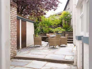 An outdoor patio area with a table and four chairs surrounded by plants and trees at Pippin Cottage in Keswick